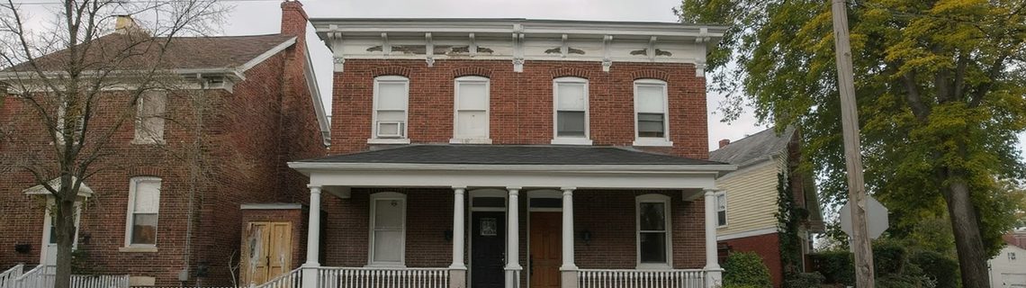 Two-story brick house with a covered front porch on a tree-lined Pennsylvania borough street