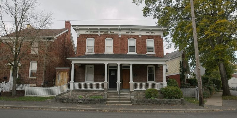 Two-story brick house with a covered front porch on a tree-lined Pennsylvania borough street