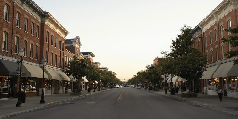 Wide main street lined with three-story brick commercial buildings and awnings at dusk